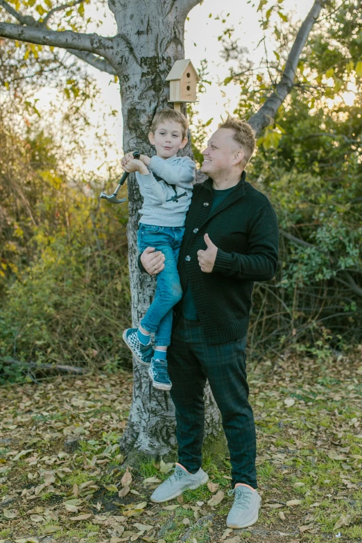 a man holding a child up to a tree, wearing jeans and a black hoodie, connor hibbs, avatar image, full - length photo