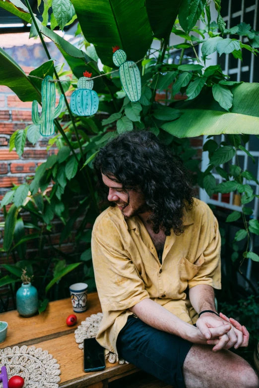 a man sitting on top of a wooden bench, an album cover, by Emily Mason, plants and jungle, portrait of danny gonzalez, with long curly, colombian