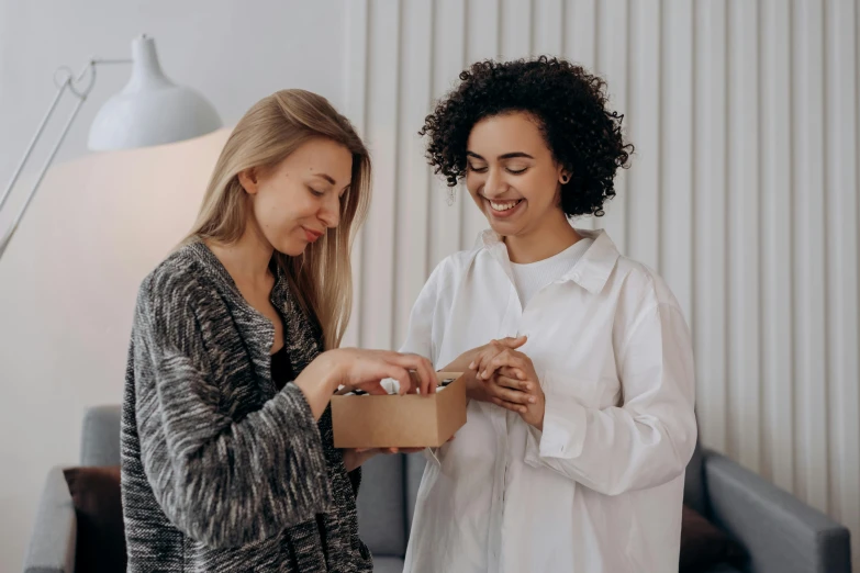 two women standing next to each other in a living room, by Emma Andijewska, pexels contest winner, hurufiyya, delivering parsel box, wearing lab coat and a blouse, avatar image, small smile