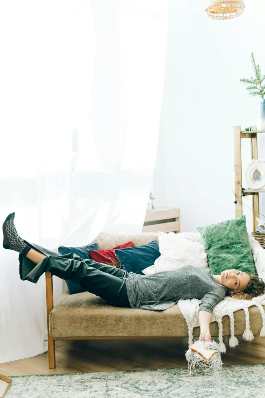 a person laying on a bed in a room, trending on pexels, happening, green corduroy pants, couch, in a white boho style studio, androgynous person