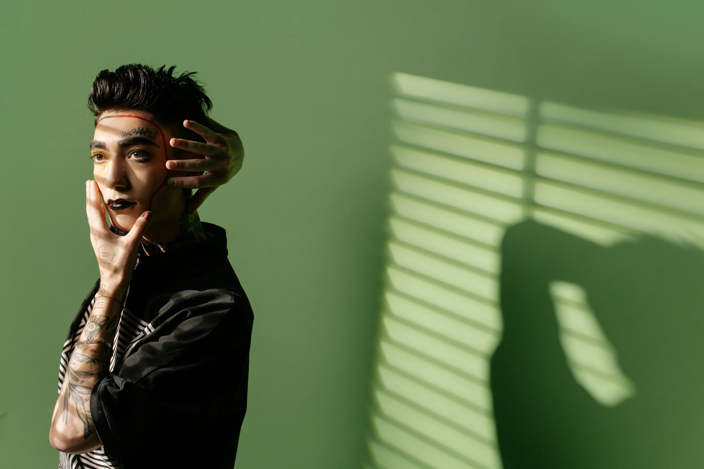 a man standing in front of a green wall, inspired by Liam Wong, pexels contest winner, photorealism, hood and shadows covering face, ashteroth, hand on cheek, studio backlight