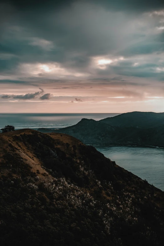a person standing on top of a mountain next to a body of water, by Thomas Wijck, pexels contest winner, sumatraism, view of the ocean, overcast dusk, “ aerial view of a mountain, late summer evening