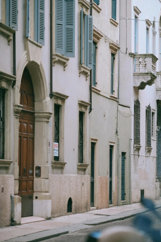 a man riding a motorcycle down a street next to tall buildings, by Melozzo da Forlì, pexels contest winner, renaissance, arched doorway, mint, quiet street, banner