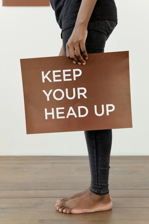 a person holding a sign that says keep your head up, by Nina Hamnett, demur, cut out, brown, sign