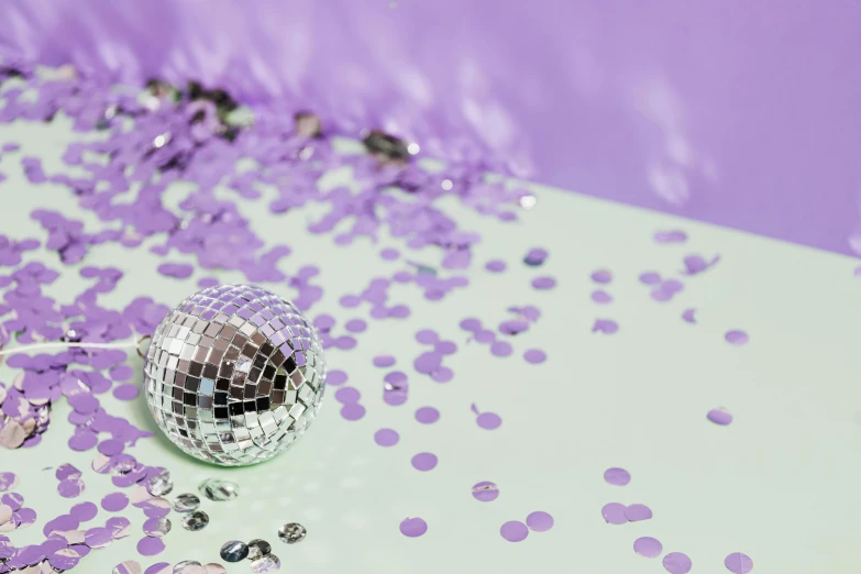 a disco ball sitting on top of a table covered in confetti, lilac, background image, white and silver, purple colour scheme