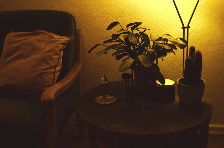 a lamp sitting on top of a table next to a chair, a still life, inspired by Elsa Bleda, unsplash, glowing plants, late night melancholic photo, yellow light, cozy candlelight