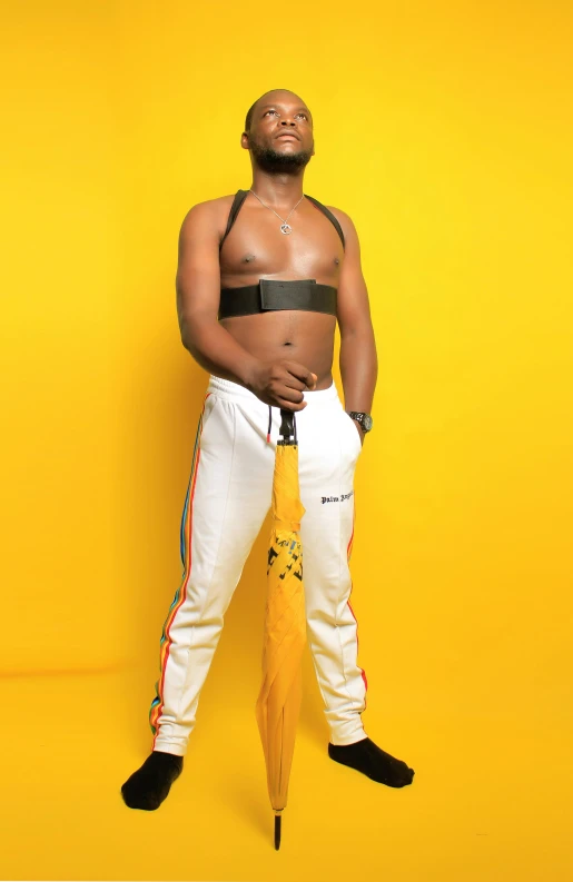 a man standing in front of a yellow wall holding an umbrella, an album cover, inspired by Ras Akyem, pexels, happening, white pants, holding a baseball bat, body harness, white background!!!!!!!!!!