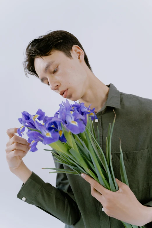 a man holding a bunch of purple flowers, an album cover, inspired by Fei Danxu, thoughtful pose, focus on iris, color photograph, large tall