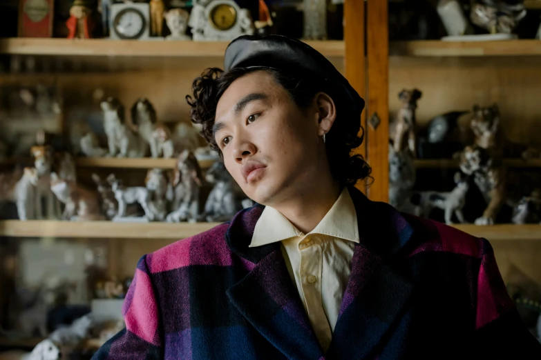 a man standing in front of a shelf filled with figurines, a portrait, by Winona Nelson, unsplash, visual art, wearing a purple detailed coat, hyung tae, wearing a beret, he is about 20 years old | short