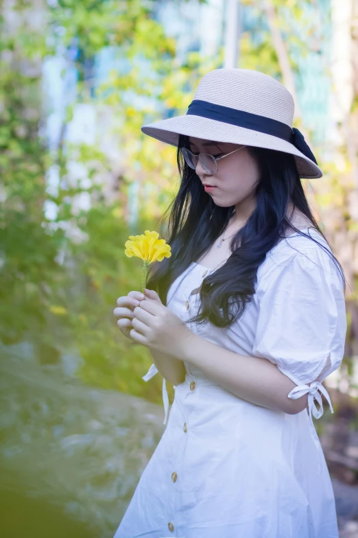 a woman in a white dress and hat holding a yellow flower, inspired by Lin Liang, unsplash, avatar image, wearing casual clothing, student, single image