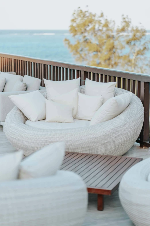 a group of white couches sitting on top of a wooden deck, circular shape, blurred background, wicker chair, bed