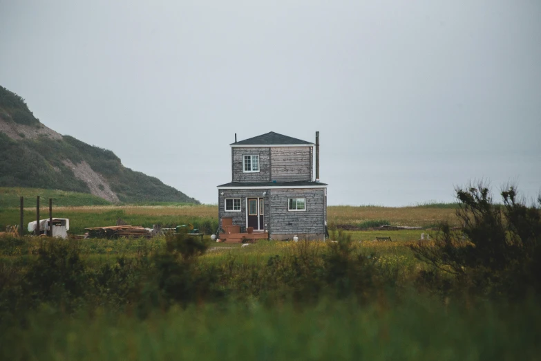 a house sitting on top of a lush green field, by Jessie Algie, pexels contest winner, on the coast, grey, cabin, post modern