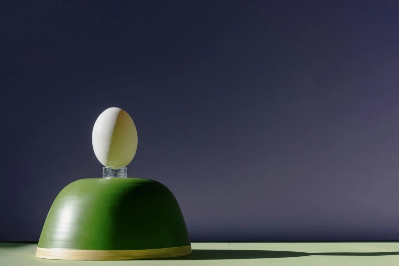 an egg sitting on top of a green bell, a surrealist sculpture, inspired by Joseph Wright of Derby, unsplash, conceptual art, round form, ignant, light on top, kek