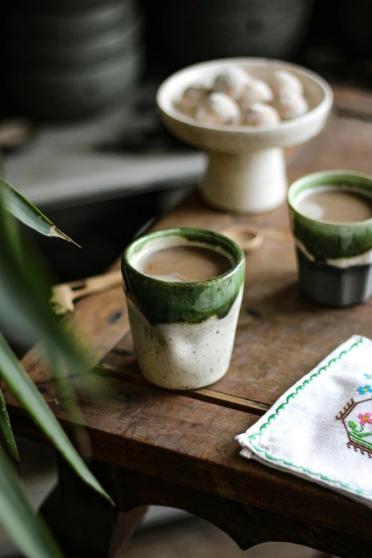 a wooden table topped with two cups of coffee, a portrait, inspired by Muggur, unsplash, renaissance, assam tea village background, #green, handmade pottery, thumbnail