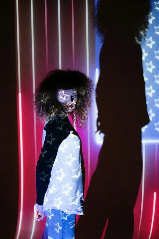 a little girl that is standing in front of a wall, inspired by Nan Goldin, unsplash, holography, stars and stripes, afro futuristic, on a mannequin. studio lighting, photo of a woman