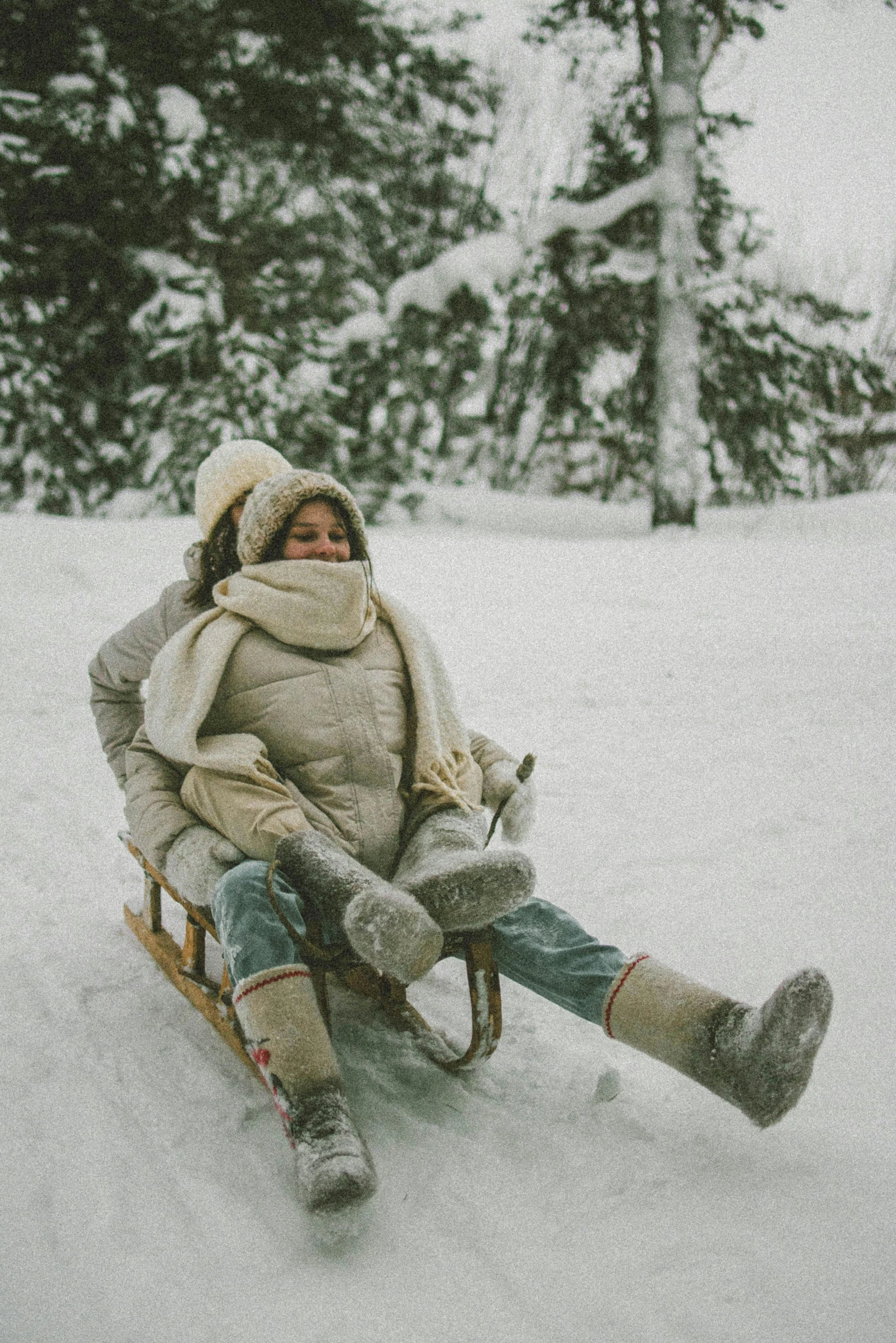 a woman riding a sled down a snow covered slope, pexels contest winner, vintage color photo, playful, grey, comfy