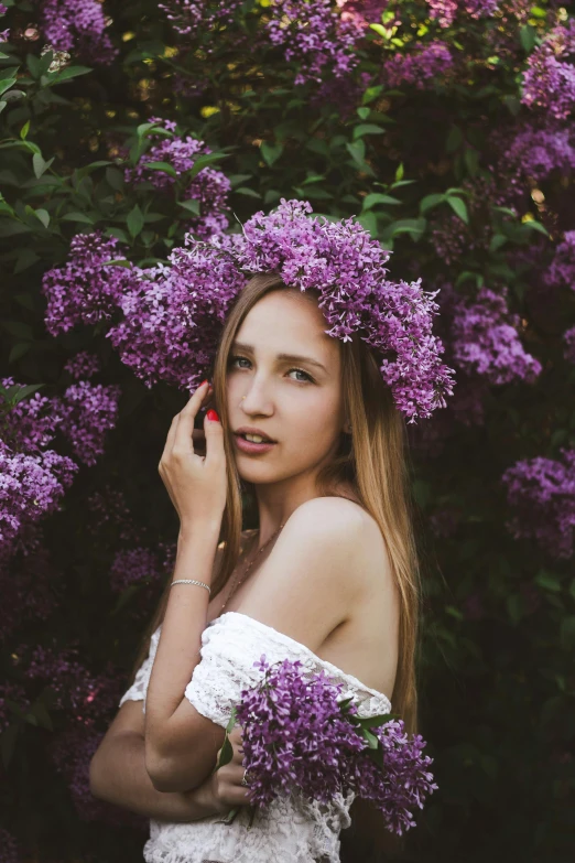 a woman standing in front of a bush of purple flowers, inspired by Elsa Bleda, pexels contest winner, handsome girl, angelina stroganova, flower crown, medium format