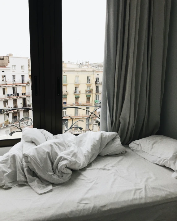 a bed sitting in a bedroom next to a window, a polaroid photo, inspired by Elsa Bleda, trending on unsplash, white marble buildings, curled up under the covers, in barcelona, thumbnail
