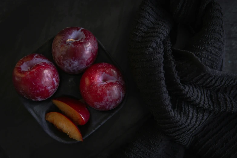 a close up of a plate of fruit on a table, a still life, inspired by Elsa Bleda, unsplash contest winner, dark purple garments, red apples, cloth wraps, on a black background