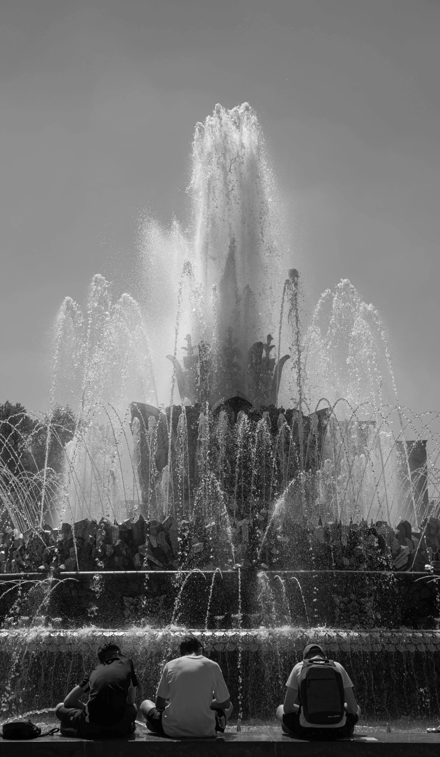 a black and white photo of people sitting in front of a fountain, a black and white photo, by Cherryl Fountain, pictured from the shoulders up, water jets, barcelona, closeup - view