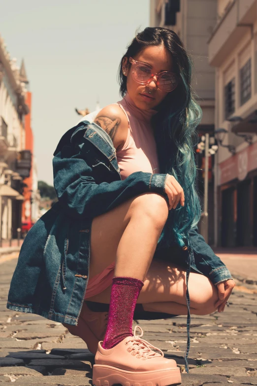 a woman squatting down on a cobblestone street, a colorized photo, inspired by Elsa Bleda, trending on pexels, hyperrealism, with pink hair, bra and shorts streetwear, young asian woman, wearing a jeans jackets