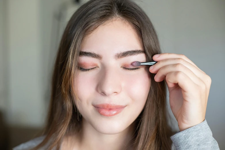 a woman is putting eyeliners on her eyes, by Julia Pishtar, trending on pexels, hailee steinfeld, soft pastels, eyes closed, textured base ; product photos