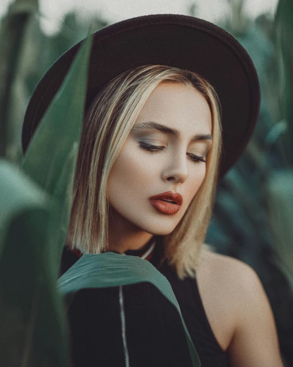 a woman wearing a hat standing in a field, inspired by Elsa Bleda, trending on pexels, sexy face with full makeup, lush foliage, dark lipstick, non binary model
