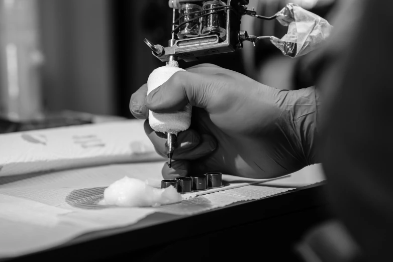 a person using a tattoo machine on a table, a black and white photo, by Mathias Kollros, unsplash, process art, fabric embroidery, surgical iv drip, medium format, cotton