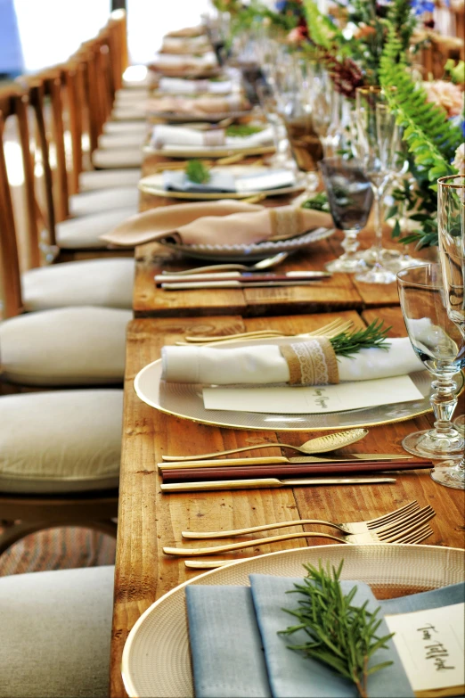 a long wooden table topped with plates and silverware, up close shot, sitting on a table, chairs, upclose