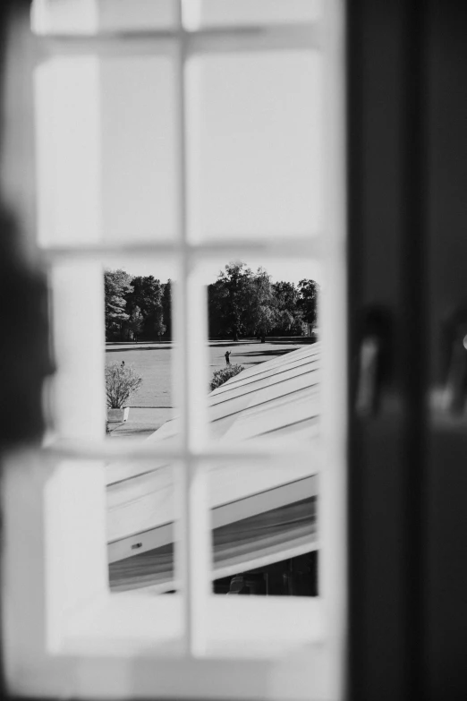 a black and white photo of a person standing in front of a window, inspired by André Kertész, unsplash, french door window, zoomed in shots, :: morning, shot from roofline