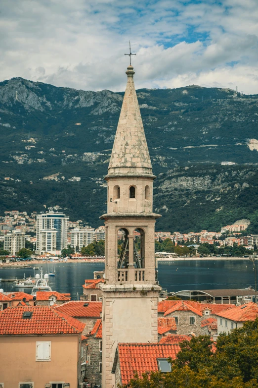 a clock tower on top of a building next to a body of water, inspired by Ivan Lacković Croata, baroque, mountains in the background, looking down from above, split near the left, lead - covered spire