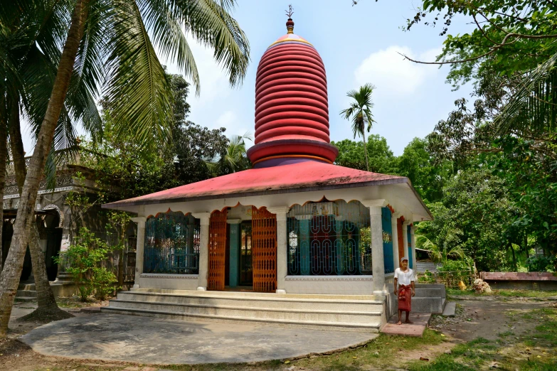 a man standing in front of a red and white building, bengal school of art, monolithic temple, lush surroundings, blue sky, puṣkaracūḍa