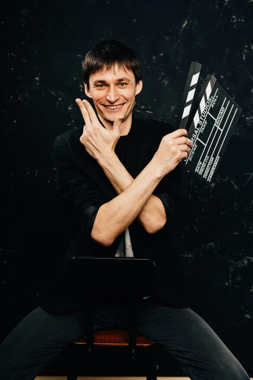 a man sitting on a chair holding a clap board, an album cover, inspired by Dmitry Levitzky, pexels contest winner, headshot profile picture, anastasia ovchinnikova, actor, finnian macmanus
