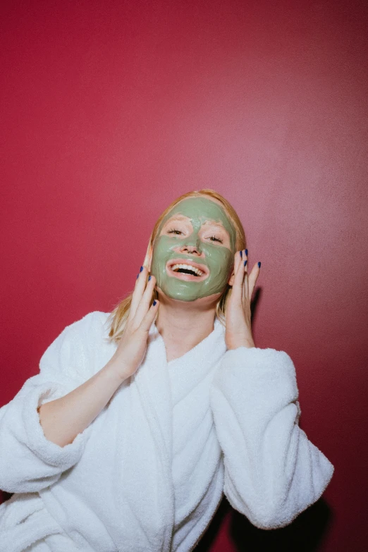 a woman putting a facial mask on her face, a colorized photo, trending on pexels, green robes, she is happy, red facial stripe, a blond