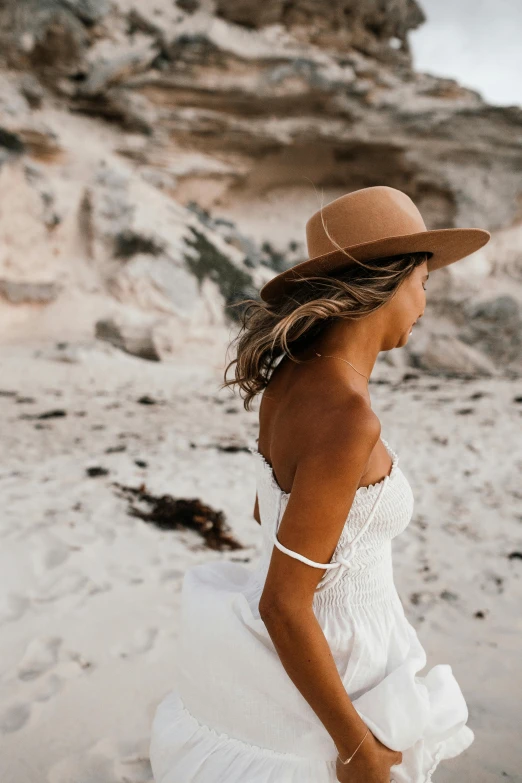 a woman in a white dress and hat on a beach, inspired by Russell Drysdale, unsplash contest winner, caramel. rugged, slightly tanned, bride, half length