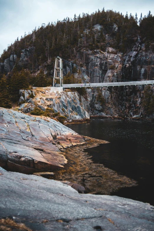 a suspension bridge over a body of water, by Brian Snøddy, pexels contest winner, rock quarry location, granite, francois legault, low quality photo