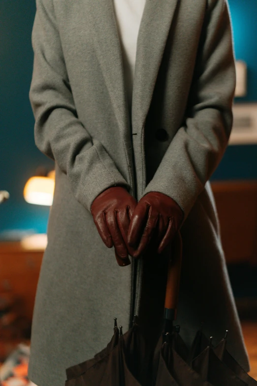 a woman in a coat and gloves holding an umbrella, inspired by Gordon Parks, unsplash, still from loki ( 2 0 2 1 ), subject detail: wearing a suit, indoor scene, leather gloves