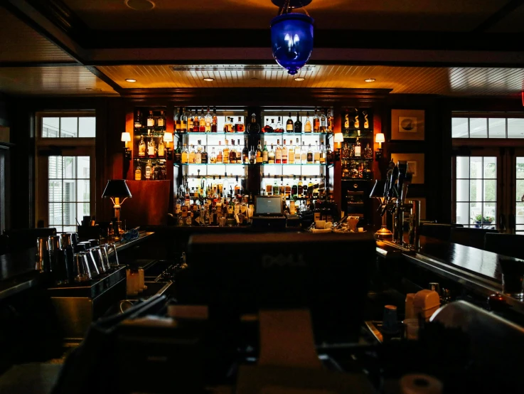 a dimly lit bar with lots of bottles on the shelves, by Carey Morris, unsplash, brightly lit blue room, colonial, upon a peak in darien, profile image