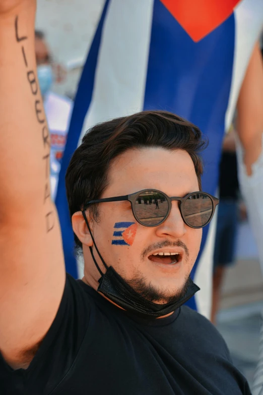 a man with a flag painted on his face, by Niko Henrichon, wearing blue sunglasses, taken in the early 2020s, diego fernandez, profile image