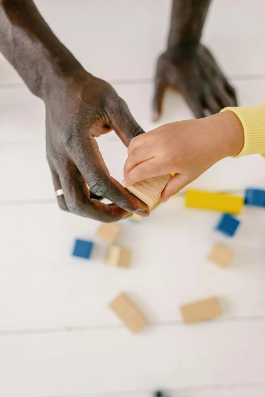 two children playing with wooden blocks on a floor, by Arabella Rankin, pexels contest winner, closeup of hand, black man, caretaker, snapchat photo