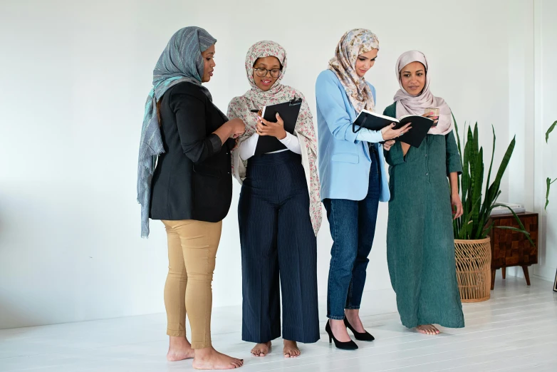 a group of women standing next to each other, trending on pexels, hurufiyya, reading a book, modestly dressed, promotional image, h 7 0 4