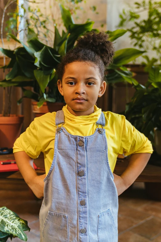 a young girl standing in front of a potted plant, pexels contest winner, yellow overall, mixed race, promotional image, schools