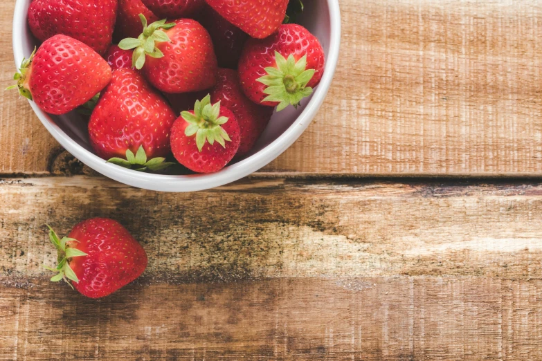 a bowl of strawberries on a wooden table, unsplash, background image, high quality product image”