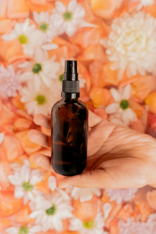 a person holding a bottle of essential oil with flowers in the background, by Julia Pishtar, rectangle, brown, thumbnail, product shot