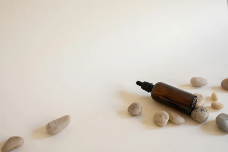 a bottle sitting on top of a table next to rocks, minimalism, acupuncture treatment, tan, white backdrop, drops around