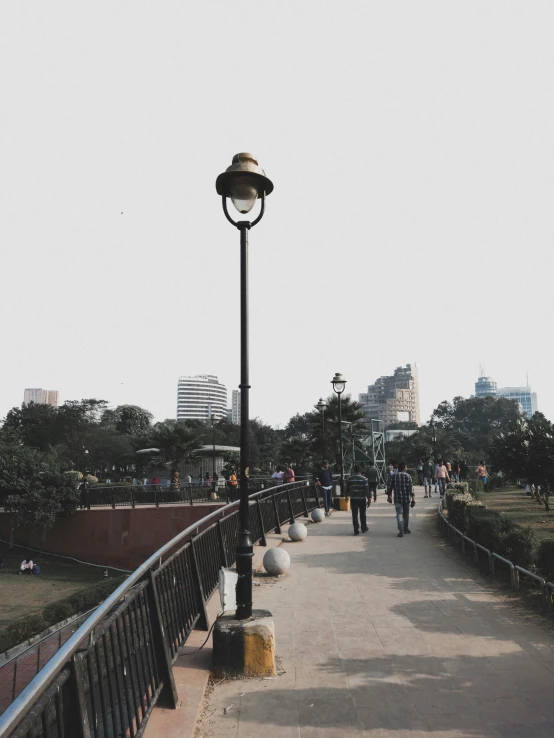 a group of people walking across a bridge, an album cover, by Alejandro Obregón, trending on unsplash, city park, lamp posts, old dhaka, background image