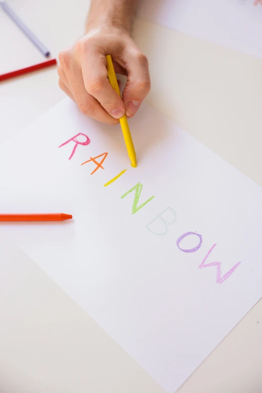 a person drawing with colored pencils on a piece of paper, a child's drawing, by Nicolette Macnamara, pexels contest winner, rainbow neon strips, style lettering, on a white table, brainbow