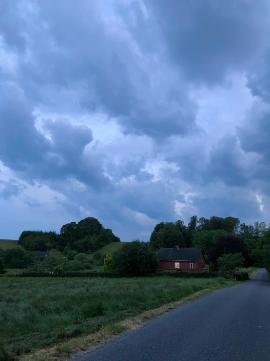 a road in the middle of a field under a cloudy sky, a picture, inspired by Gerard Soest, happening, next to a farm house and a barn, dark night stormcloud, looking towards camera, image from afar