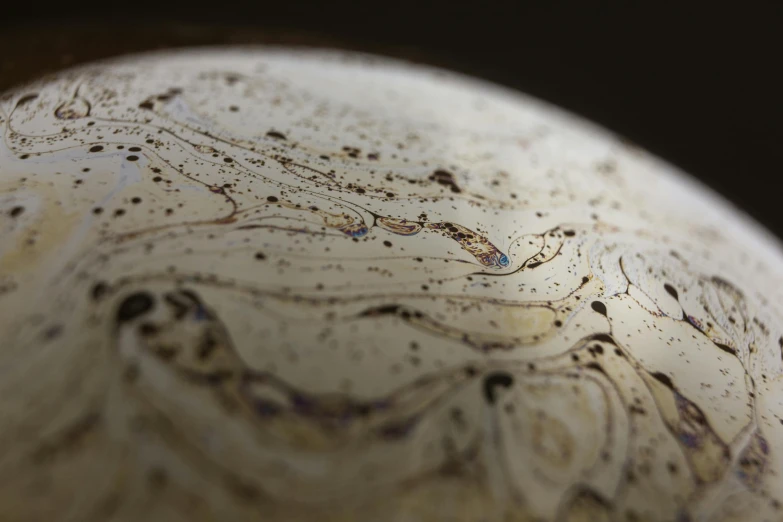 a white vase sitting on top of a wooden table, a macro photograph, inspired by Lucio Fontana, process art, large globe, ancient swirls, brown, speckled