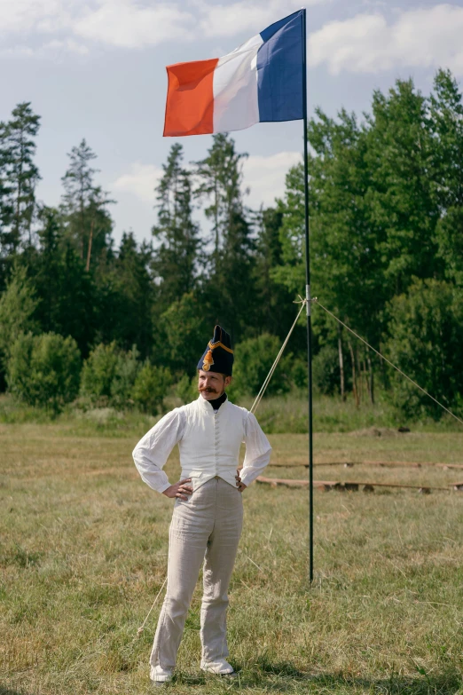 a man standing in a field next to a flag, inspired by Horace Vernet, unsplash, renaissance, white uniform, camp, full color photograph, finland